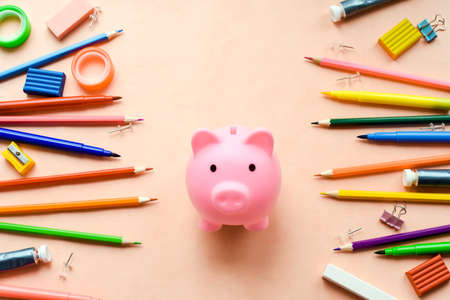 saving for education or back to school concept, piggy bank and colorful marker, pencil and pen on pink background.の写真素材