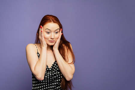 Surprised happy young female stands on purple background, glad to see big discounts on clothes,...