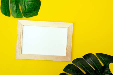 Top view of a white square frame mockup with palm leaf decoration. Summer composition on yellow background.の写真素材