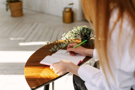 A beautiful woman writes in a blank notebook at her desk at home.の写真素材