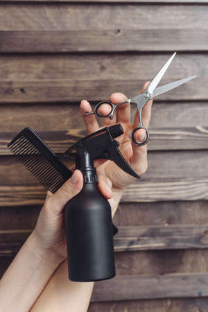 Hairdresser tools on a wooden background in the hands of a master. Dark tint. Protective spray, comb and hair scissors.の写真素材
