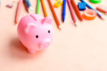 Office supplies next to a piggy bank on a pink background. The concept of accumulating money for school or college.の写真素材