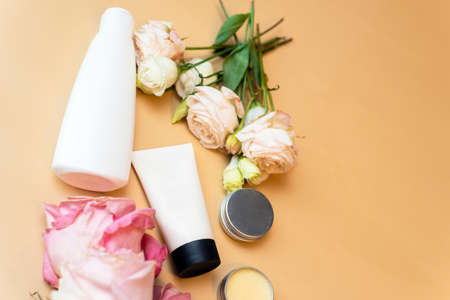 Cream and lotion in white tubes on a beige background with flowers of roses. Cosmetic products for...