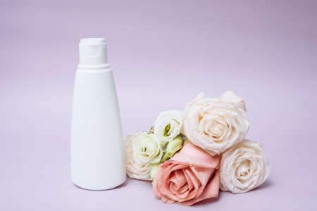 Moisturizing body lotion in a white tube next to a rose flower on a pink background. Copy space.