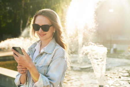 Attractive young woman with curly hair using her touch screen mobile cell phone by the fountain.の写真素材