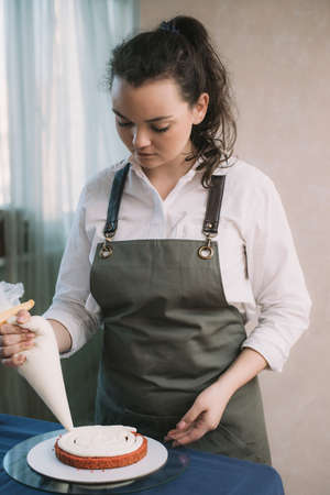 The hands of a bakers girl squeeze pink cream onto a cake base.の写真素材