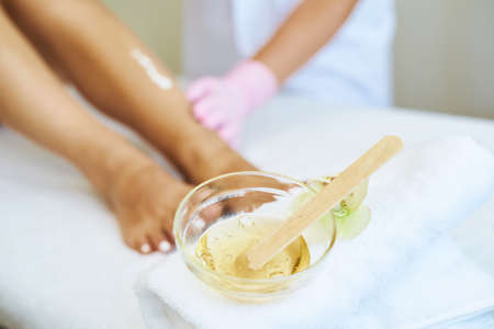 Cosmetologist is doing depilation. The procedures at the beautician. A jar of wax in the foreground.の写真素材