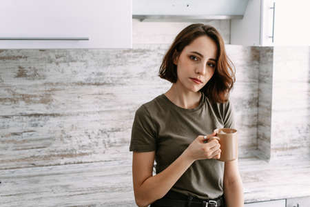 A lovely woman is drinking a warm drink in her kitchen.