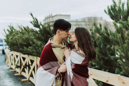 Beautiful young couple stand face to face among christmas tree. Young newlyweds in love, gently...