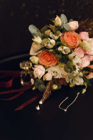 Wedding bridal bouquet of roses next to the brides jewelry - uepochki and earrings on red velvet. Wedding and love concept.の写真素材