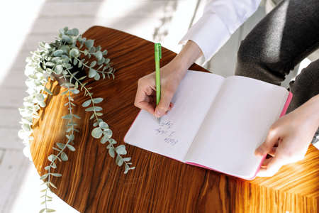 Mans hand writes in a notebook on a light desk.