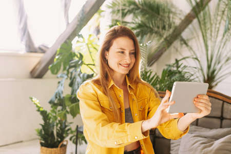 A beautiful woman sits at home among a large number of plants and communicates with relatives or friends using a tablet.の写真素材