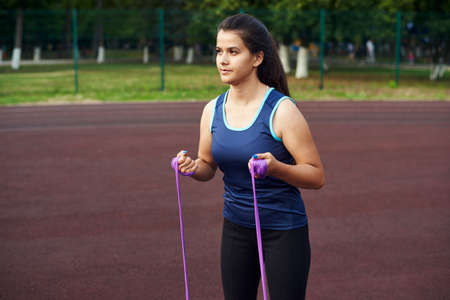 A beautiful woman shakes the muscles and muscles in her arms with the help of an expander and fitness elastic bands. Cute girl goes in for sports on the street.の写真素材