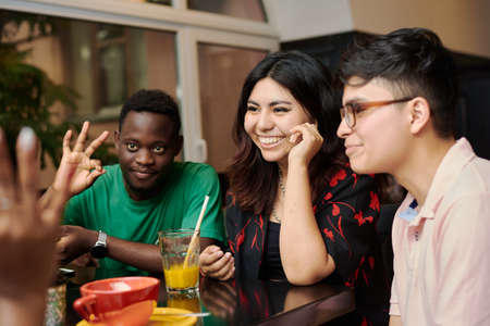 Multiracial happy young people drink coffee at cafe, black and white cheerful mates laughing enjoying drinks having fun sitting together at restaurant table, diverse friends share lunch at meeting.の写真素材