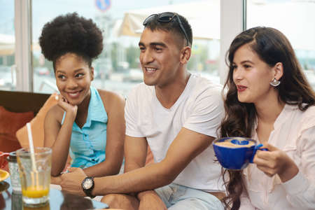 Multiracial happy young people drink coffee at cafe, black and white cheerful mates laughing...