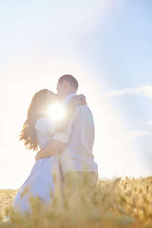 Stylish and modern couple kissing in a wheat field. A young woman hugs her boyfriend and kisses each other. The concept of passion and love. Out of focus.の写真素材