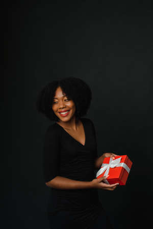 Happy black young woman with afro is holding a holiday gift in her hands and smiling. Gift giving and Christmas shopping concept. Black Friday.の写真素材