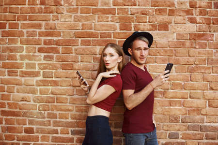 The couple is using the phone. Woman and man stand with their backs to each other on the phone.