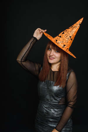 Smiling young woman in orange hat and witch costume on black background. Copy space.の写真素材
