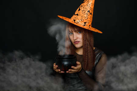 Photo of a young woman in a conical hat holding an artificial pot in the studio.
