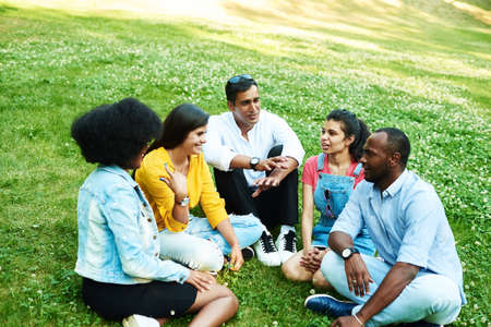Afghan, black, mexican and indian chatting while sitting in the park on the grass. The concept of communication of different nationalities.の写真素材