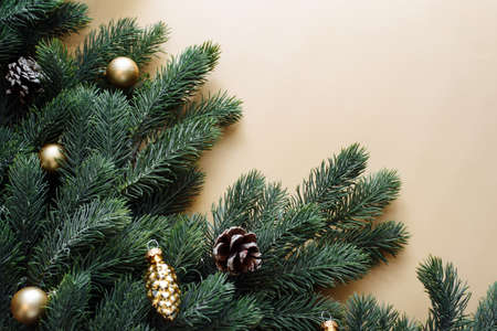 Space for text between Christmas tree branches with Christmas gold decorations and balls on a beige...