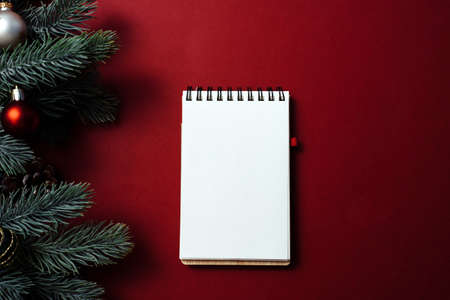 Christmas red background with blank notebook, pen, fir tree branches and red decorations. Christmas,...