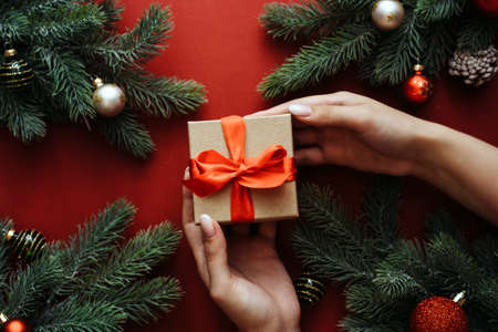 Craft gift with a red ribbon in the hands of a young girl with a nude manicure next to the branches...