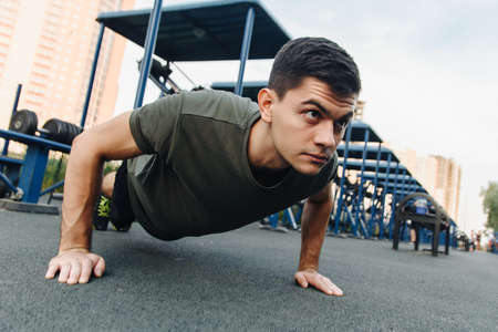 A young man does push-ups on the street on a specialized sports ground with trainers. Build muscles in the fresh air. Sport and healthy lifestyle concept.の写真素材