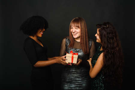 Image of beautiful three young woman rejoicing while standing with present box isolated over black...
