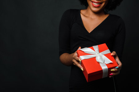 A dark-skinned woman with an afro hairstyle gives a gift to the camera. The concept of New Years shopping, gifts. Copy space.の写真素材