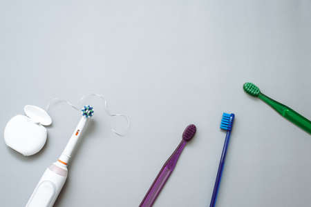 Electric toothbrush, floss and colored disposable toothbrushes on grey