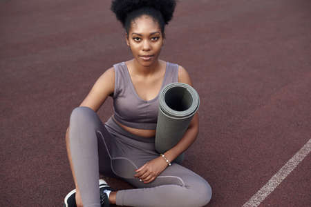 Dark-skinned beautiful girl is ready for yoga in a sports outdoor stadium. Young woman goes in for sports outdoors.の写真素材