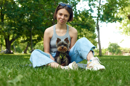 Cute beautiful woman with little Yorkshire Terrier in a park outdoors. Lifestyle portrait.の写真素材