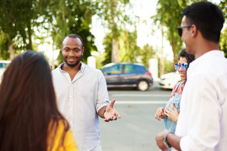 Young people having fun outdoors. A group of multi-ethnic friends are talking and laughing while standing in the street.の写真素材