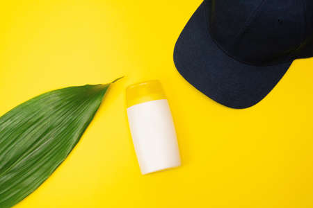 A suncream and cap are on the yellow background. Sun protection products with tropical, palm leaf.の写真素材