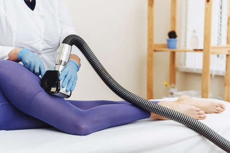 Woman in special purple suit getting anti cellulite massage in a spa salon. Lpg massage procedure. Hands of therapist holding lipomassage tool.の写真素材