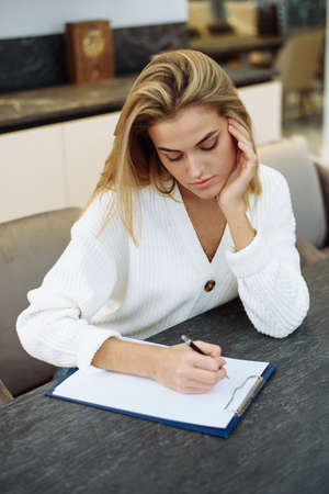 A lovely young woman is sitting at the table in her kitchen and writing in a notebook. Making a home...