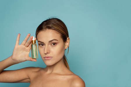 A beautiful young woman moisturizes her skin with a serum. Caring for the skin.の写真素材