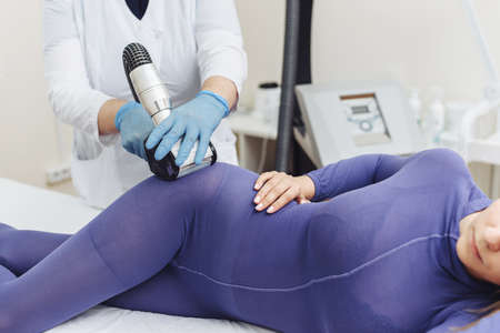 Woman in special purple suit getting anti cellulite massage in a spa salon. Lpg massage procedure. Hands of therapist holding lipomassage tool.の写真素材