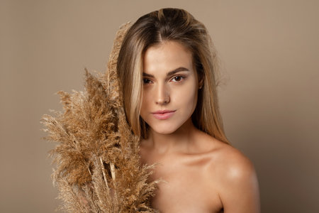Lovely young female model with loose hair holds dry pampas grass in her hands. The concept of natural cosmetics from wheat grains. Skin care.の写真素材