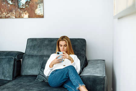 Relax on the couch at home. Lifestyle. Attractive woman using smart phone while sitting on the sofaの写真素材