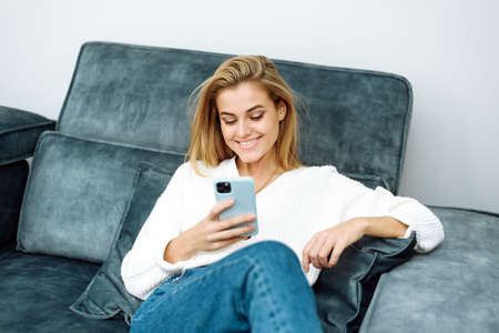 Smiling young woman surfing the internet and buying things while sitting on the couch at home. Online shoppingの写真素材
