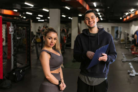 A young sports trainer discusses a nutrition plan with a beautiful client in the gym. The concept of...