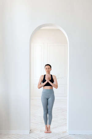 A young woman practices yoga, prays and comprehends Zen in the arch of a bright room. The concept of...