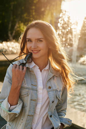 Beautiful portrait of a young girl in casual clothes on a fountain background. Sunny summer portrait...