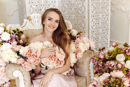 Young lady Caucasian white woman with blonde high-heeled hairstyle and bare shoulders posing with different colors in studio interiors with sofaの写真素材