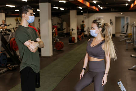 A sports coach and a young woman wearing masks chat in the gym during a pandemic. Sports activities.  protectionの写真素材