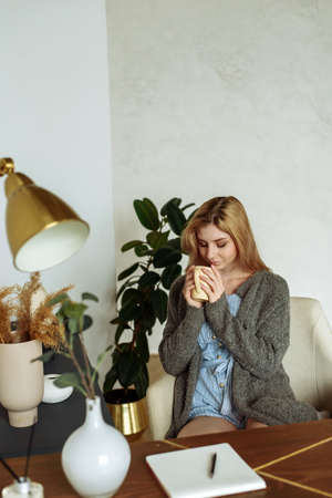 A cute young woman makes notes in a notebook while sitting at her desk at home and drinking coffeeの写真素材