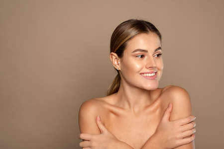 Young lovely woman is touching her shoulder. Beautiful face of young woman with clean fresh skin close up on beige background. Skin care face . Cosmetologyの写真素材